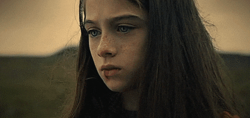 a young girl with long dark hair and freckles is looking at the camera .