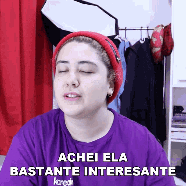a woman wearing a purple shirt and a red hat says " achei ela bastante interessante "