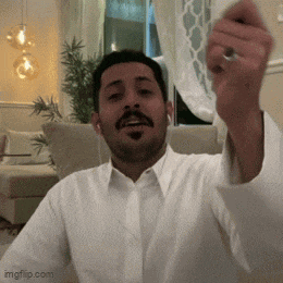 a man in a white shirt is sitting on a couch with his hand up in the air