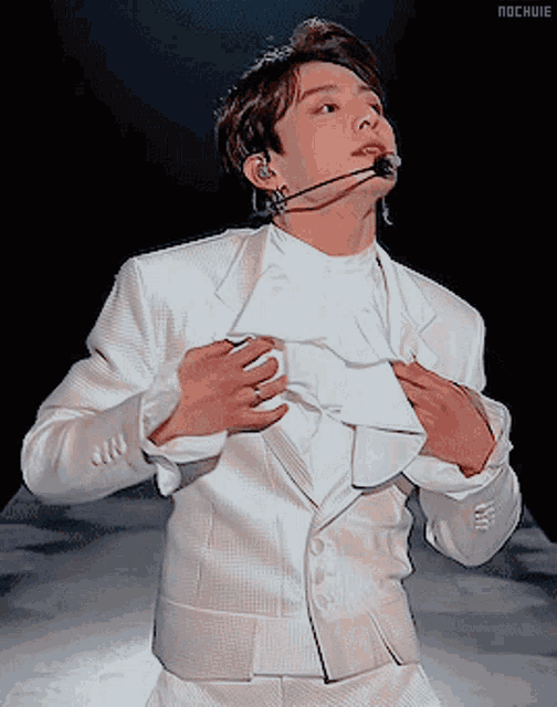 a young man in a white suit with a microphone in his ear