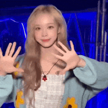 a woman with blonde hair is wearing a blue sweater and a necklace and making a funny face .