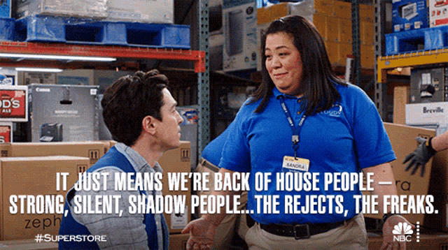 a man and a woman are talking in a warehouse and the woman is wearing a blue shirt that says sasha