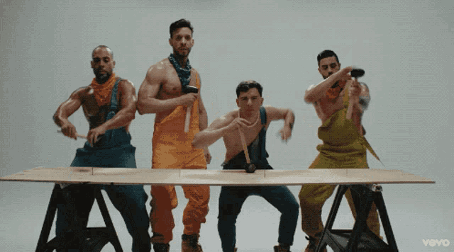 a group of men in overalls are standing around a table with the word vevo on the bottom right