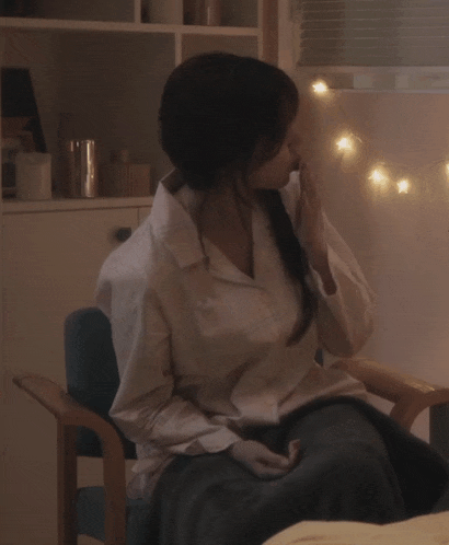 a woman in a white shirt is sitting in a chair in front of a window