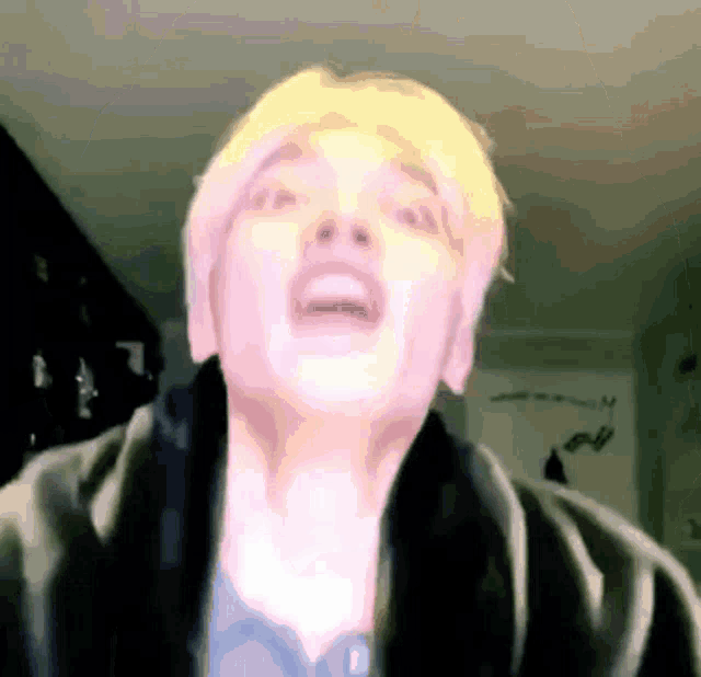 a man with blonde hair is making a funny face while wearing a black jacket .