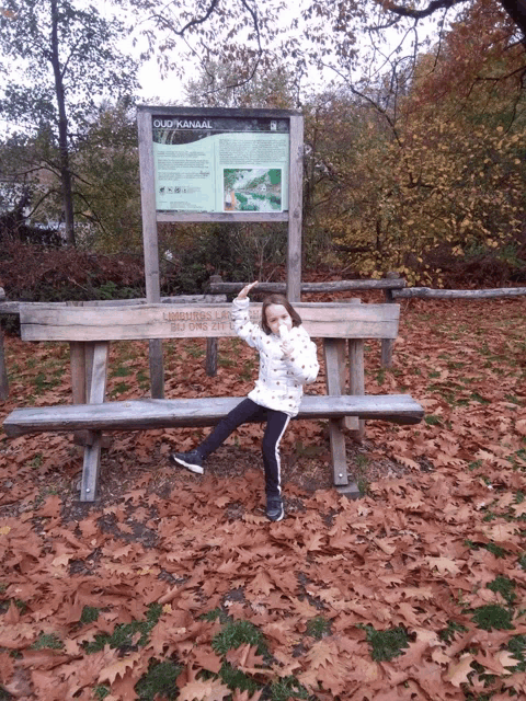 a little girl sitting on a wooden bench in front of a sign that says oud-kanaal