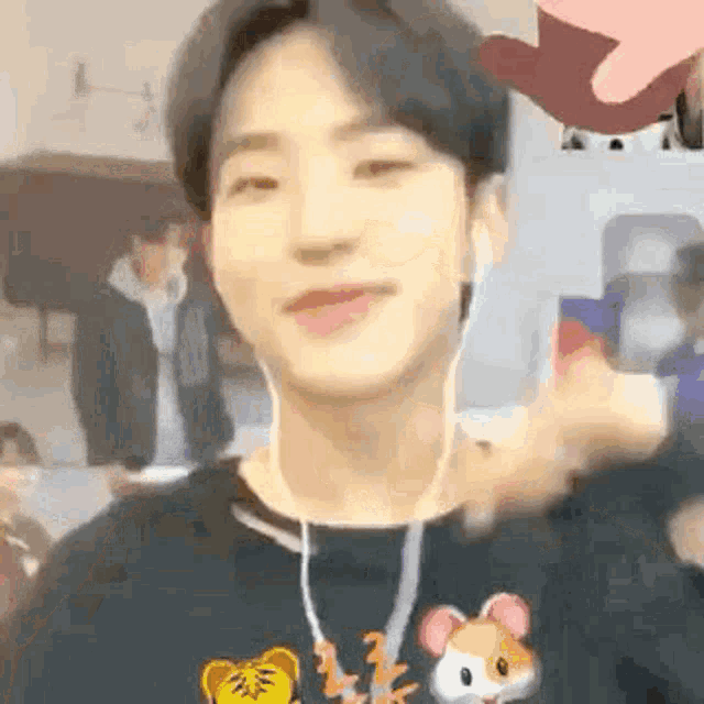 a young man wearing headphones and a black sweater with a hamster on it is smiling .