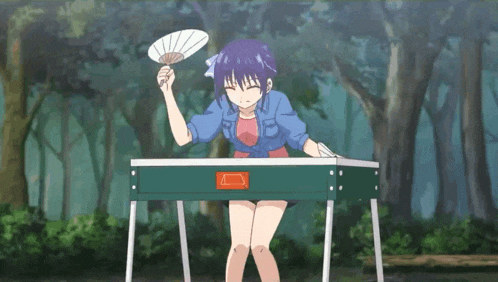 a girl in a blue shirt is holding a fan while standing next to a table