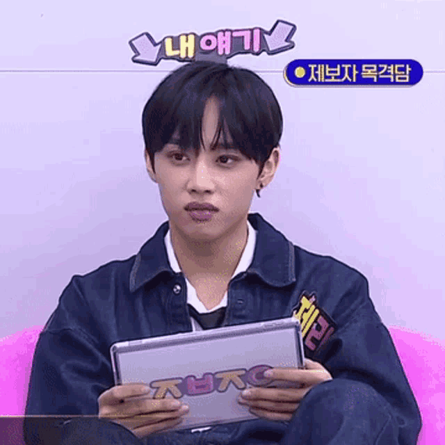 a young man sitting on a pink couch holding a tablet that says ' lh oh ' on top of his head