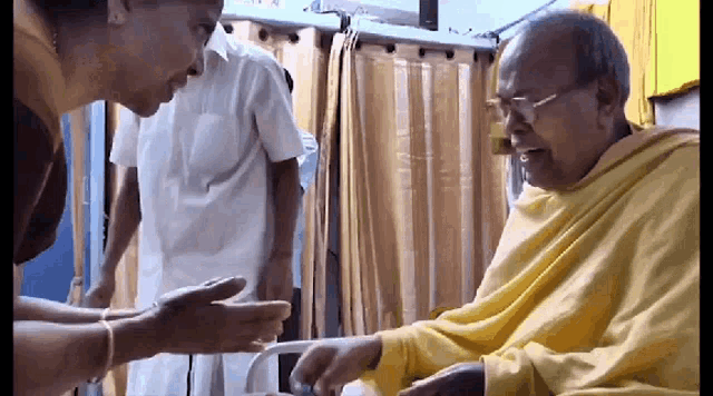 a man in a yellow robe is talking to a woman in a hospital room