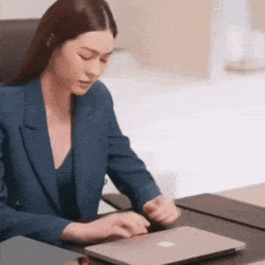 a woman in a suit is sitting at a desk with a laptop .