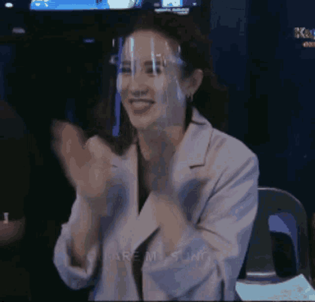 a woman wearing a face shield is clapping her hands in a room .