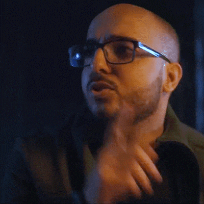 a bald man with glasses and a beard is making a shhh gesture