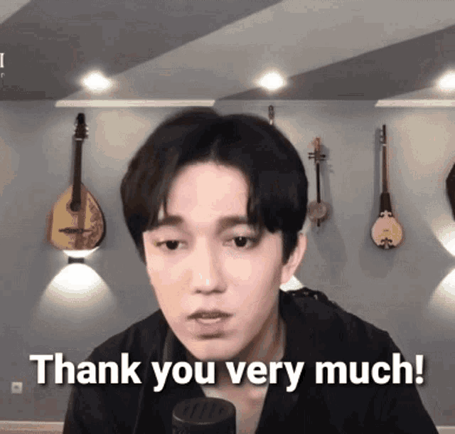 a man says thank you very much in front of a wall of guitars