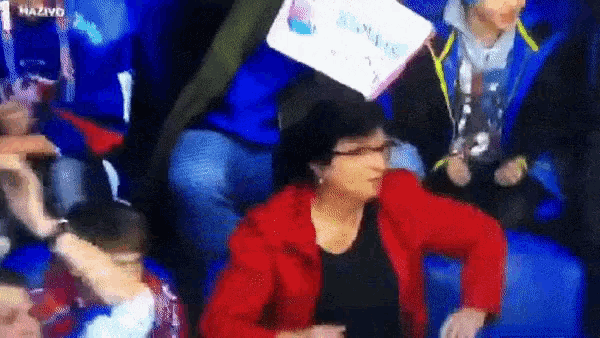 a woman in a red jacket is sitting in a crowd with a sign that says ' hazivd ' on it