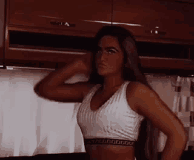 a woman is standing in a kitchen wearing a white crop top .