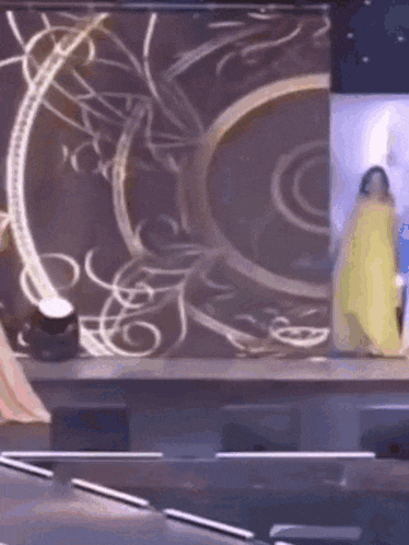 a woman in a yellow dress is standing on a stage in front of a screen .
