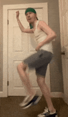 a man in a white tank top and shorts is dancing in front of a white door .