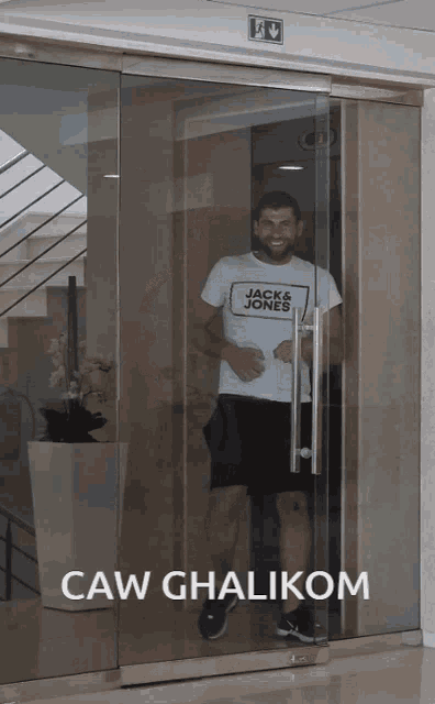 a man wearing a white jack & jones shirt is standing in a glass doorway