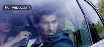 a man is sitting in the driver 's seat of a car looking out the window .