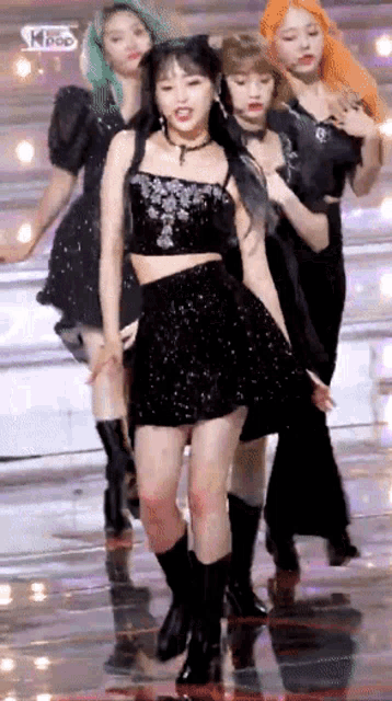 a group of girls are dancing on a stage and one of them is wearing a black dress and boots