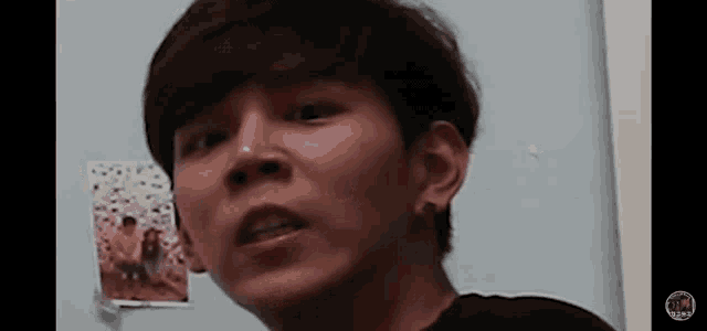 a close up of a young man 's face with a picture on the wall behind him