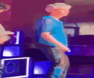 a man in a blue shirt is dancing in front of a sign that says ' pc ' on it