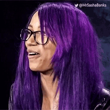 a woman with purple hair and glasses is smiling and looking at the camera .
