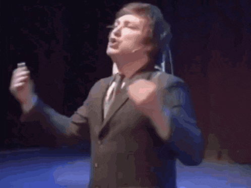 a man in a suit and tie is singing into a microphone while standing on a stage .