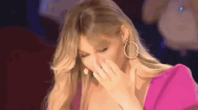 a woman is covering her mouth with her hand while wearing a pink dress and hoop earrings .
