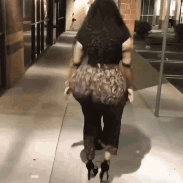a woman is walking down a sidewalk wearing heels and a snake print skirt