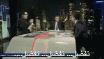 a group of men are sitting at a table with arabic writing on the screen
