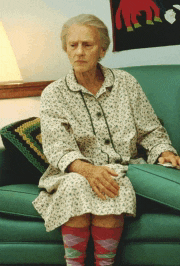 an elderly woman sits on a green couch wearing socks