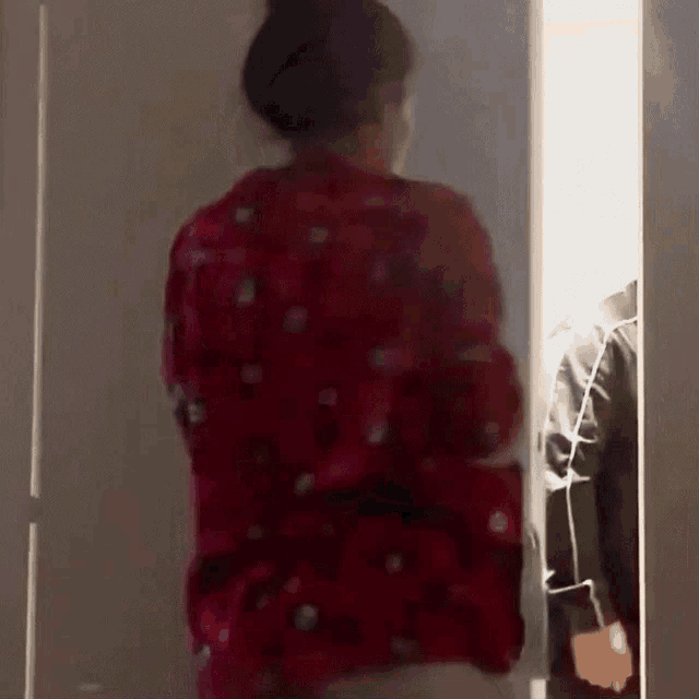 a woman in a red shirt is standing in a doorway looking at a man in a black jacket .