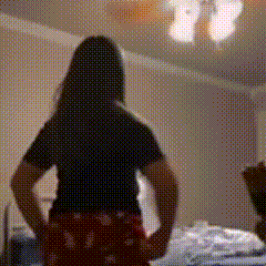 a woman is standing in a bedroom with her hands on her hips and a chandelier in the background .