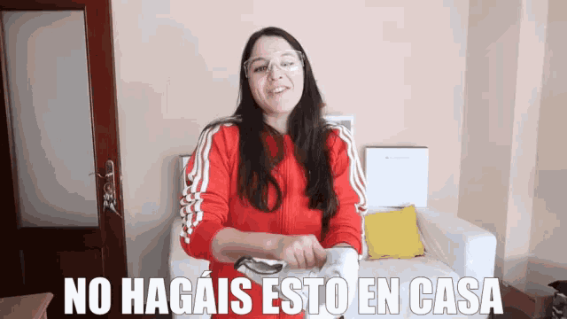 a woman wearing glasses and a red jacket is sitting on a couch with the words no hagais esto en casa