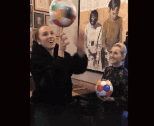 two women playing with balloons in front of a painting of a man