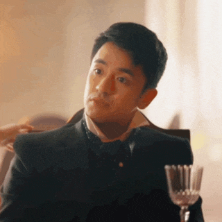 a man in a suit and tie is sitting at a table with a glass of wine in front of him