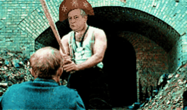 a man wearing a hat and holding a bat talks to another man