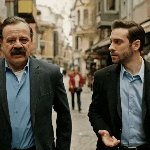 a man with a mustache talks to another man on a street