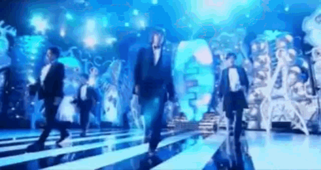 a group of men in tuxedos are dancing on a stage in front of a blue light .