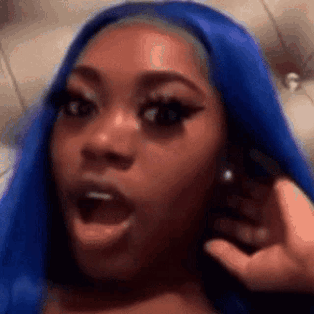 a woman with blue hair is making a surprised face while talking on a cell phone .