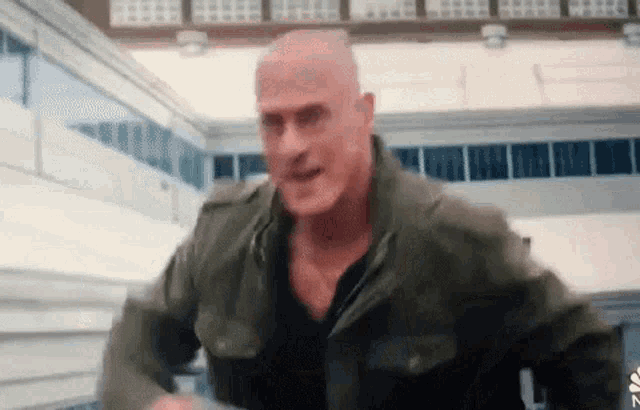 a bald man wearing a green jacket is running in a building .