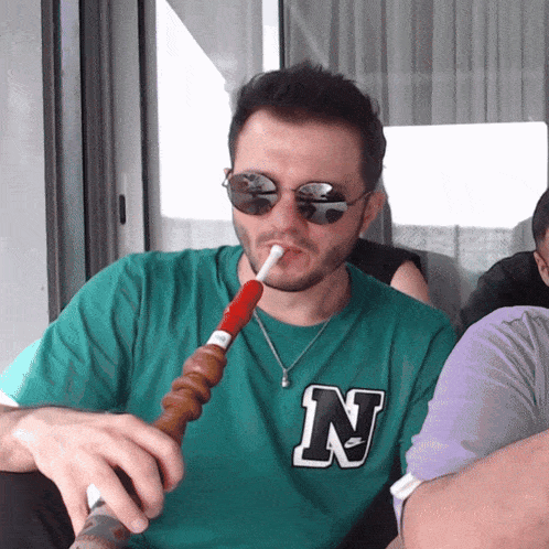 a man wearing a green shirt with the letter n on it is smoking a hookah