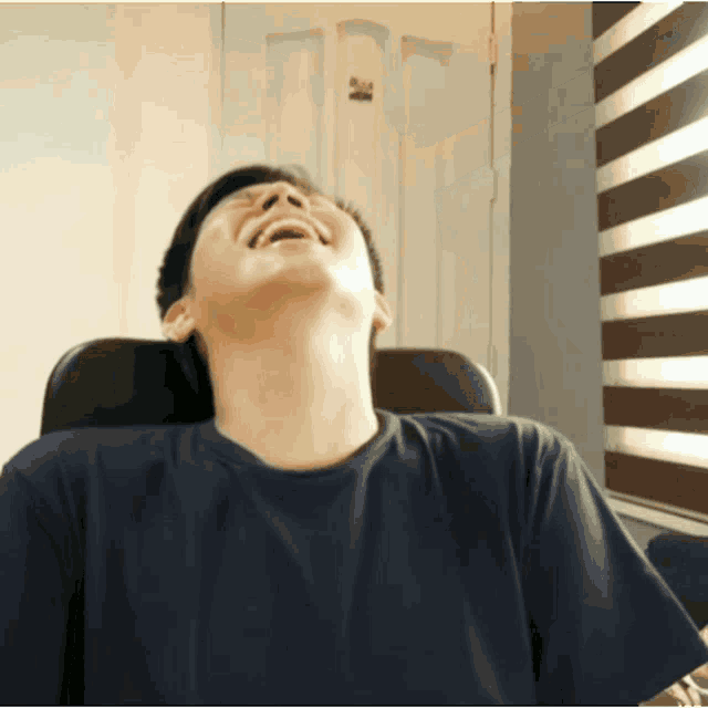 a man in a blue shirt is laughing in front of a striped blind