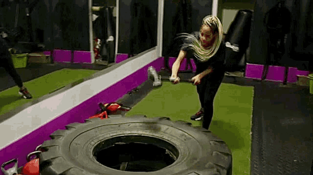 a woman is throwing a tire in a gym .