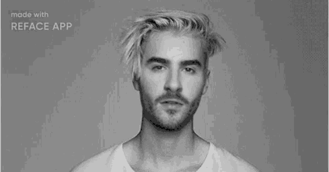 a man with blonde hair and a beard is wearing a white shirt and looking at the camera in a black and white photo .