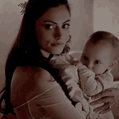 a woman is holding a baby in her arms and looking at the camera .