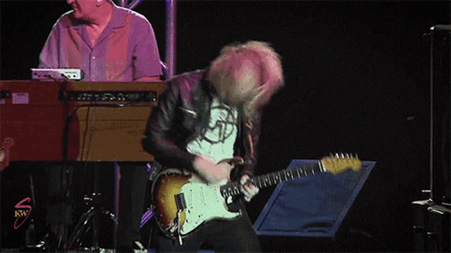 a man playing a guitar on a stage in front of a keyboard that says rw on it