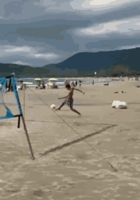 a boy is kicking a soccer ball on a beach with mountains in the background